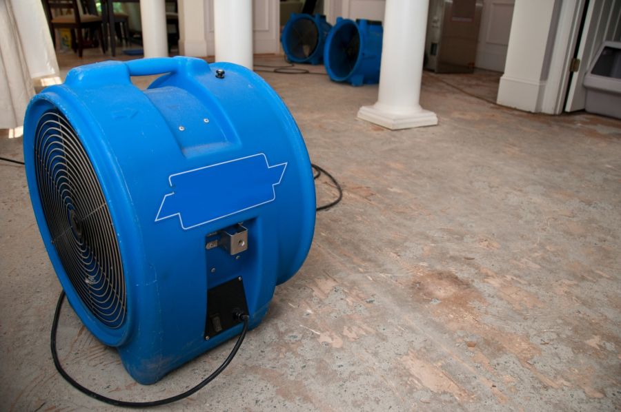 Blue industrial air movers drying a water-damaged floor in a building interior